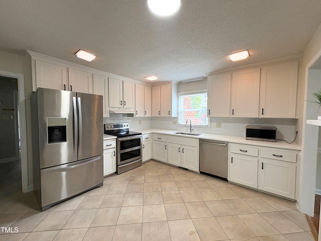 kitchen with a sink, decorative backsplash, light countertops, under cabinet range hood, and appliances with stainless steel finishes