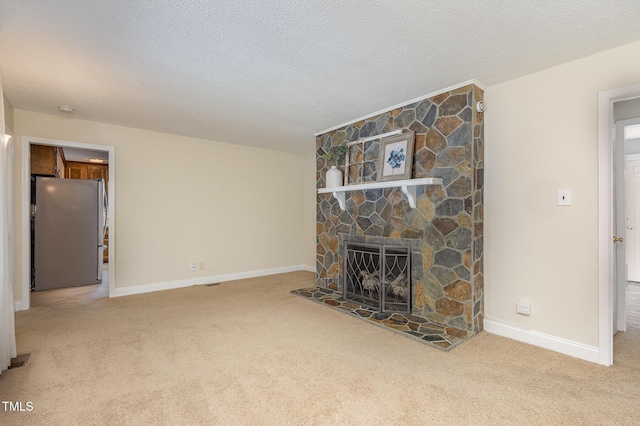 unfurnished living room with carpet, a stone fireplace, baseboards, and a textured ceiling