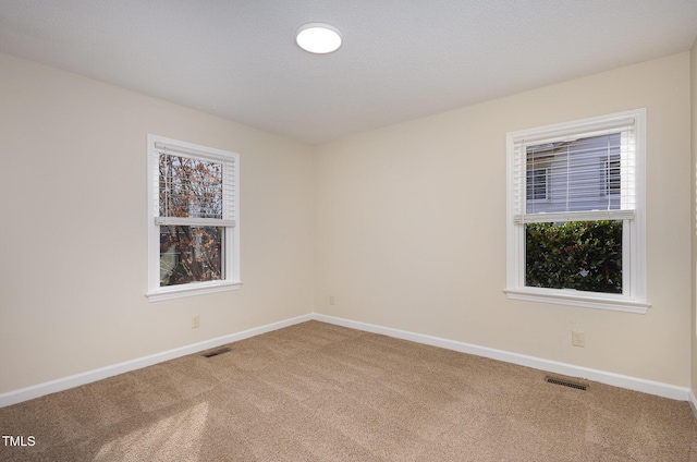 carpeted spare room with visible vents, baseboards, and a healthy amount of sunlight