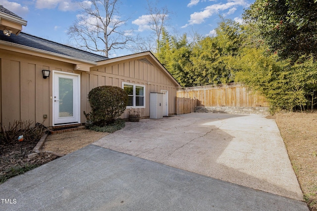 exterior space with board and batten siding, fence, a shingled roof, and a patio area