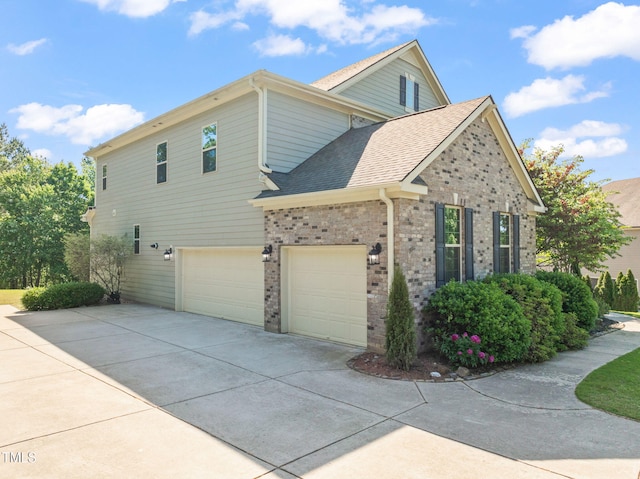 view of side of property with brick siding, driveway, a shingled roof, and a garage