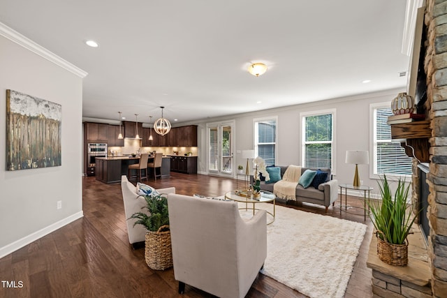living area with a fireplace, baseboards, dark wood-style floors, a chandelier, and ornamental molding