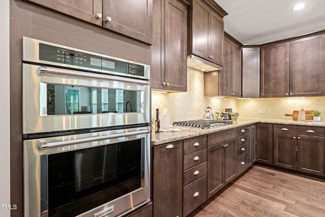 kitchen with dark brown cabinetry, appliances with stainless steel finishes, decorative backsplash, and light wood finished floors