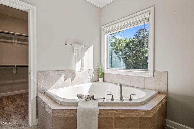 bathroom with baseboards, a bath, and a spacious closet