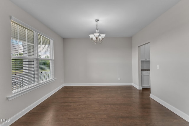 empty room with dark wood finished floors, baseboards, and a notable chandelier