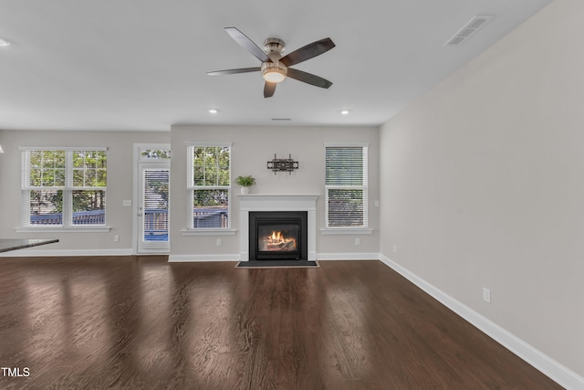 unfurnished living room with a fireplace with flush hearth, wood finished floors, visible vents, baseboards, and ceiling fan