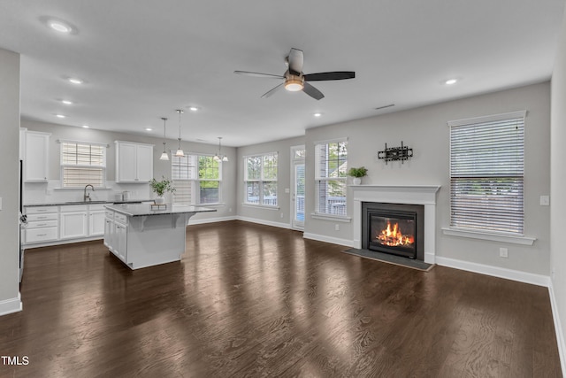 unfurnished living room featuring a fireplace with flush hearth, a sink, plenty of natural light, baseboards, and a ceiling fan