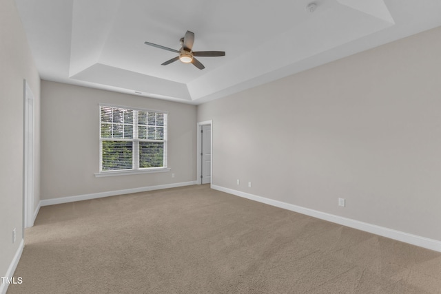 empty room with a tray ceiling, carpet, a ceiling fan, and baseboards