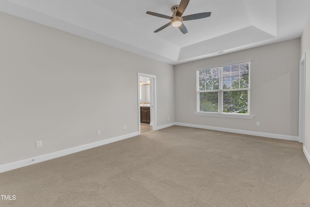 empty room with a tray ceiling, a ceiling fan, baseboards, and light carpet