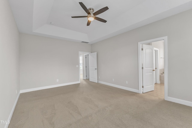 unfurnished bedroom with a tray ceiling, carpet, visible vents, and baseboards