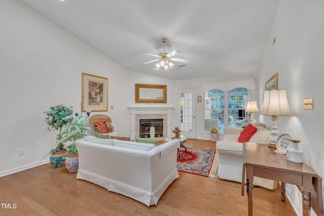 living room featuring a ceiling fan, wood finished floors, a high end fireplace, baseboards, and lofted ceiling