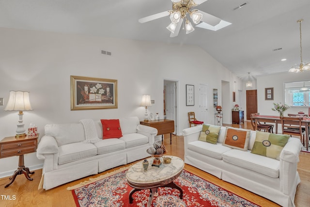 living area featuring wood finished floors, visible vents, lofted ceiling with skylight, and ceiling fan