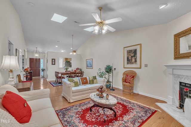living room with light wood finished floors, a high end fireplace, a ceiling fan, lofted ceiling with skylight, and baseboards