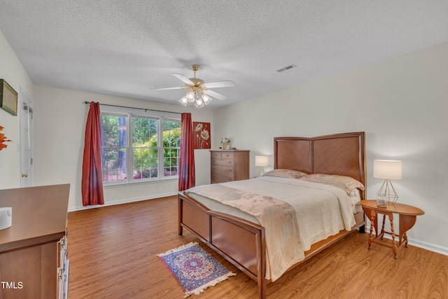 bedroom with a textured ceiling, baseboards, visible vents, a ceiling fan, and wood finished floors