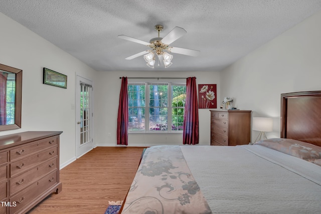 bedroom with a textured ceiling, light wood-type flooring, ceiling fan, baseboards, and access to exterior
