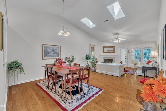 dining area featuring a skylight, light wood-type flooring, a fireplace, baseboards, and visible vents
