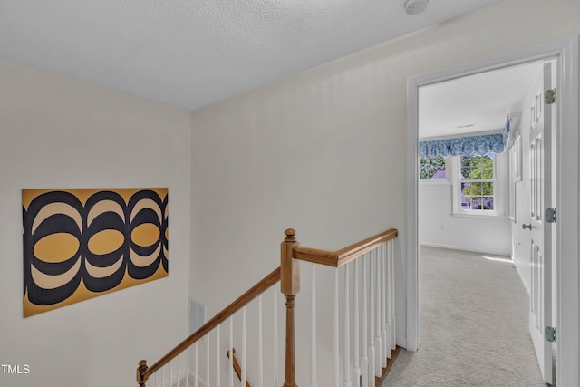 corridor with carpet floors, a textured ceiling, baseboards, and an upstairs landing