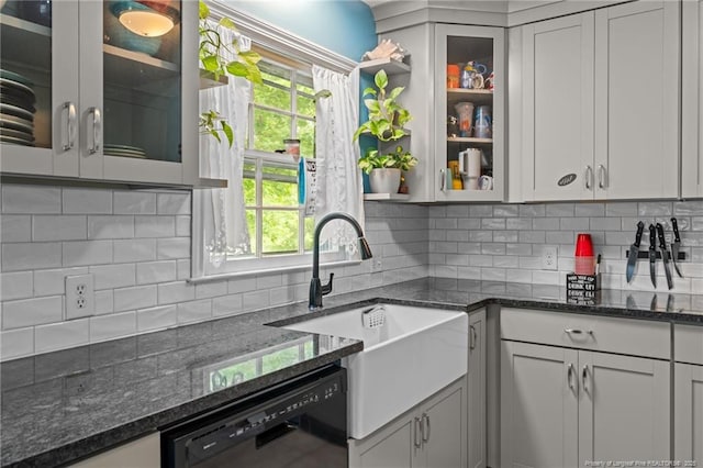 kitchen featuring dishwasher, tasteful backsplash, a sink, dark stone countertops, and glass insert cabinets