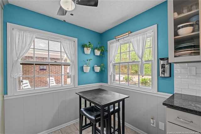 dining area with wainscoting, a textured ceiling, ceiling fan, and tile patterned floors