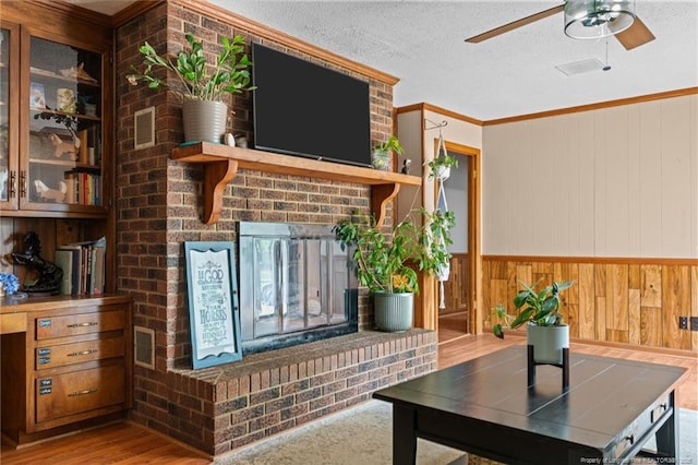 living room with wooden walls, ceiling fan, a brick fireplace, crown molding, and wood finished floors