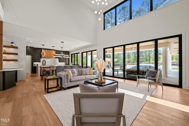 living room featuring an inviting chandelier, a high ceiling, light wood-style floors, and a wealth of natural light
