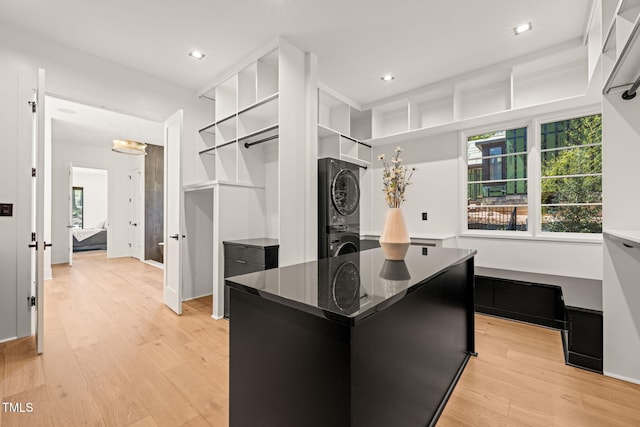 kitchen featuring a center island, open shelves, light wood finished floors, dark cabinetry, and stacked washer and clothes dryer