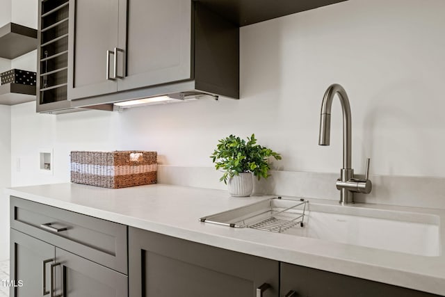 kitchen with a sink, light countertops, gray cabinets, and open shelves