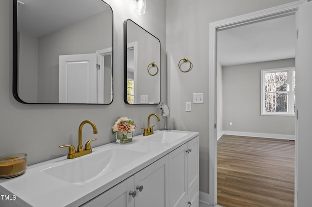 full bath featuring double vanity, baseboards, a sink, and wood finished floors