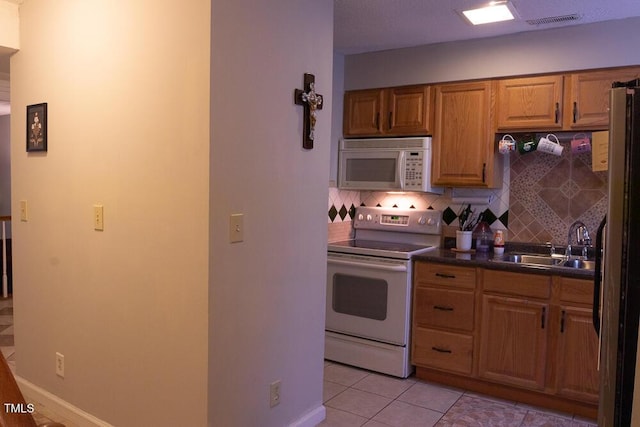 kitchen featuring a sink, dark countertops, visible vents, backsplash, and white appliances
