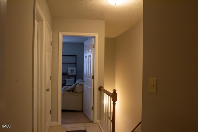 corridor with light tile patterned flooring, a textured ceiling, baseboards, and an upstairs landing