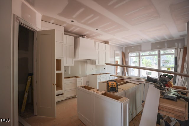 kitchen with white cabinets, a kitchen island, washer / clothes dryer, and custom range hood
