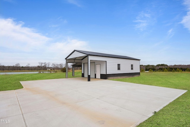 view of outdoor structure featuring concrete driveway, a water view, an outbuilding, and a carport