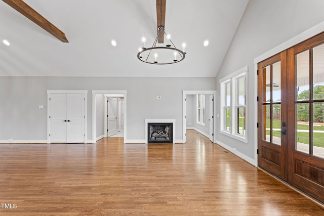 unfurnished living room with recessed lighting, light wood finished floors, french doors, beamed ceiling, and a chandelier