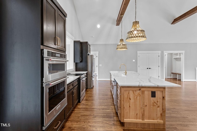 kitchen with baseboards, appliances with stainless steel finishes, beamed ceiling, and a kitchen island with sink