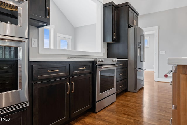 kitchen with dark wood-style flooring, stainless steel appliances, light countertops, baseboards, and lofted ceiling
