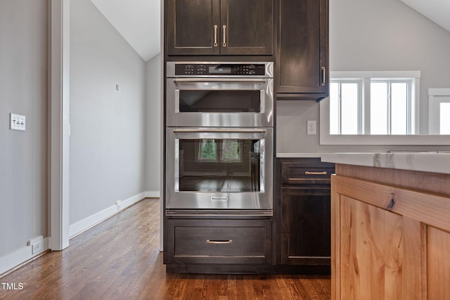 kitchen featuring double oven, vaulted ceiling, dark brown cabinetry, and dark wood-style flooring