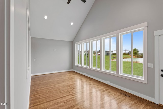 spare room featuring wood finished floors, a water view, a ceiling fan, and baseboards