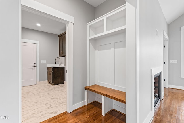 mudroom featuring a fireplace, baseboards, wood finished floors, and a sink