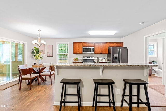 kitchen with an inviting chandelier, appliances with stainless steel finishes, light wood finished floors, and brown cabinets