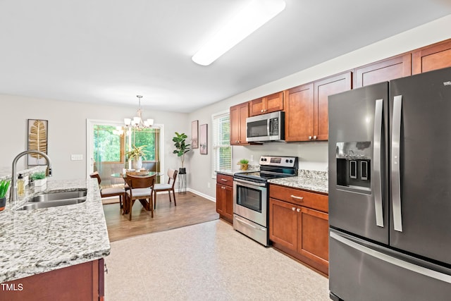 kitchen with a sink, appliances with stainless steel finishes, brown cabinets, and a notable chandelier