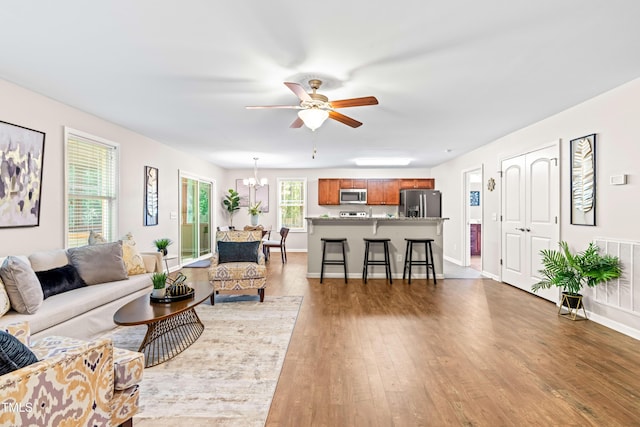living room with baseboards, ceiling fan with notable chandelier, wood finished floors, and visible vents