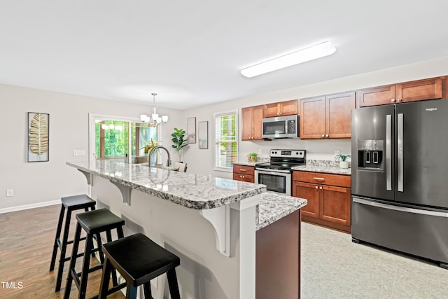 kitchen with hanging light fixtures, a notable chandelier, appliances with stainless steel finishes, a breakfast bar, and a center island with sink