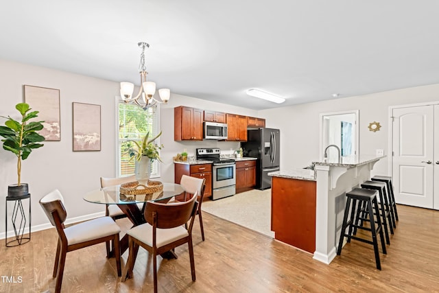 kitchen with brown cabinetry, light wood finished floors, a notable chandelier, a breakfast bar, and stainless steel appliances