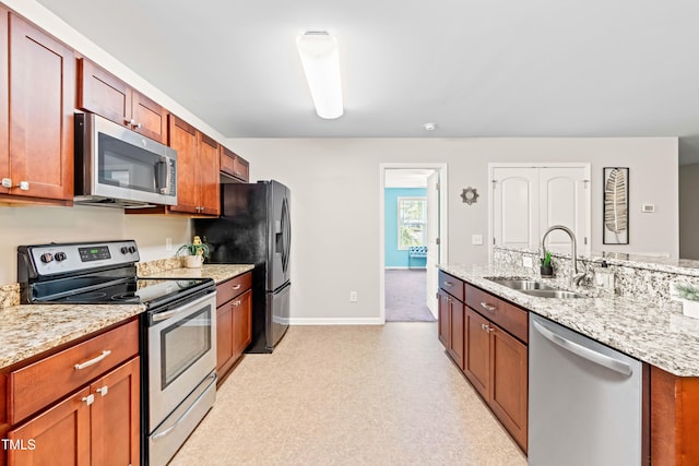 kitchen with appliances with stainless steel finishes, light stone countertops, a sink, baseboards, and light floors