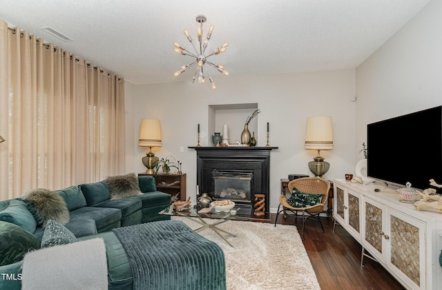 living area featuring dark wood-style flooring, a glass covered fireplace, a chandelier, and visible vents