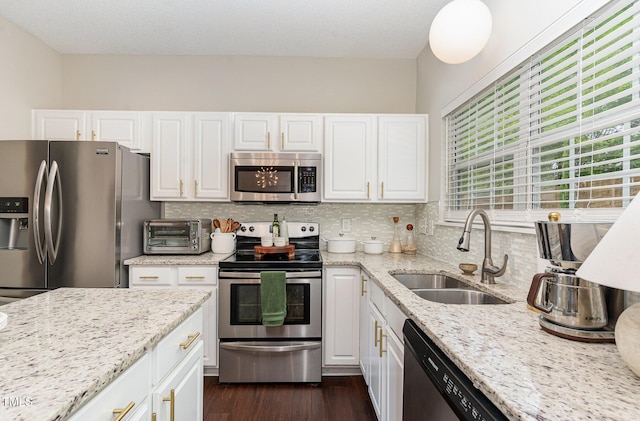 kitchen with appliances with stainless steel finishes, a toaster, white cabinetry, and a sink