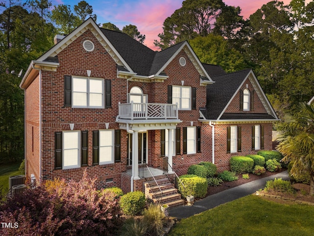 view of front of house with a lawn, a shingled roof, a balcony, and brick siding