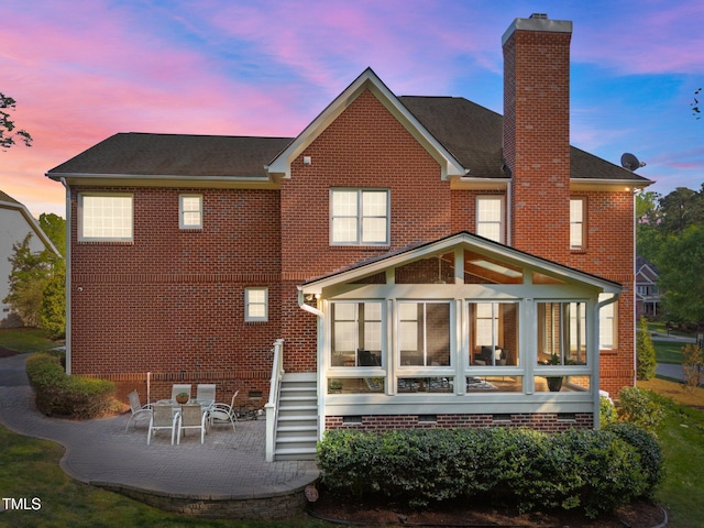 rear view of house featuring brick siding, crawl space, a chimney, a patio, and a sunroom