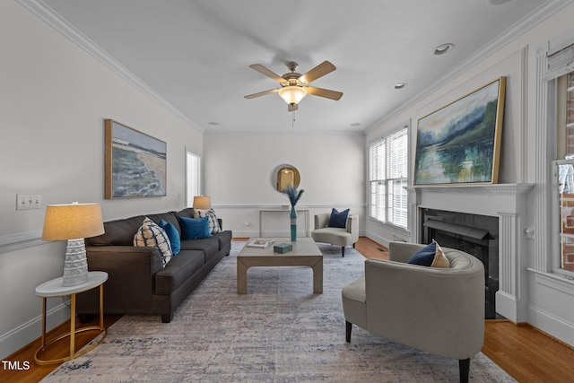 living area with baseboards, wood finished floors, ceiling fan, crown molding, and a fireplace