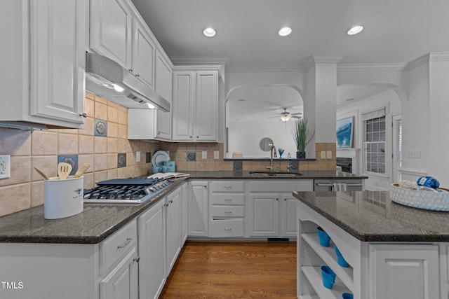 kitchen with a sink, ceiling fan, arched walkways, white cabinets, and under cabinet range hood